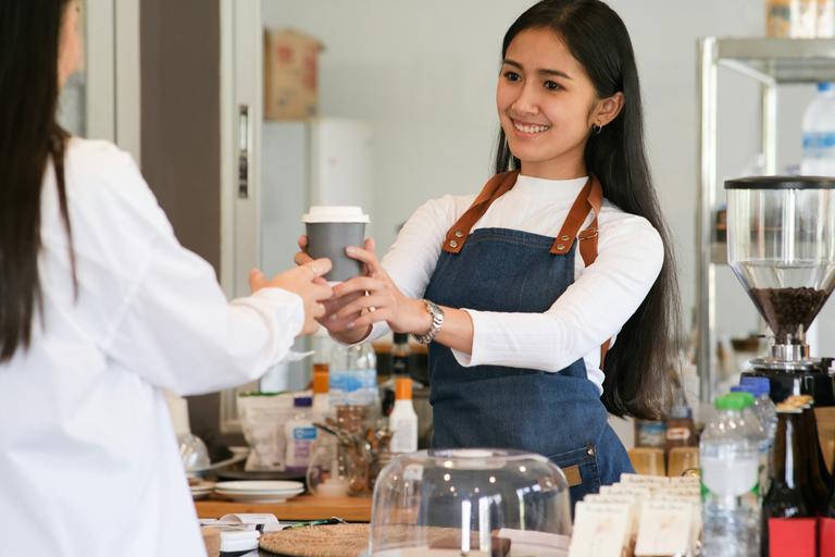 A cafe employee handing coffee to a customer.